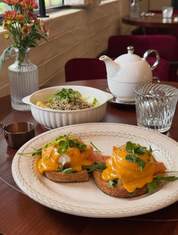 Plate of food on a table with a teapot and flowers in the background