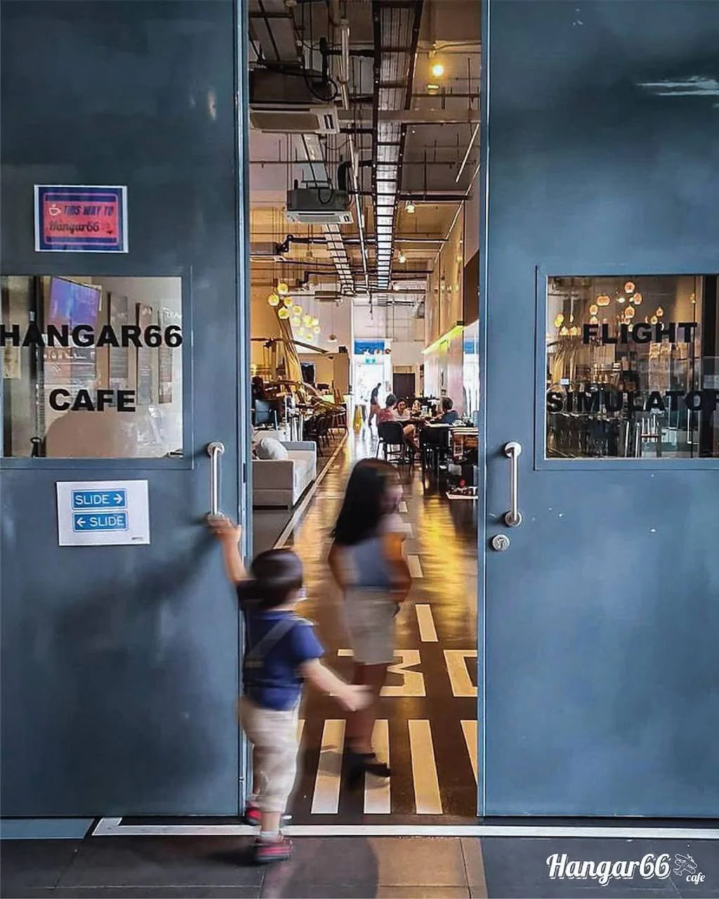 Child opening a door to a cafe named 'Hangar66' with interior visible.